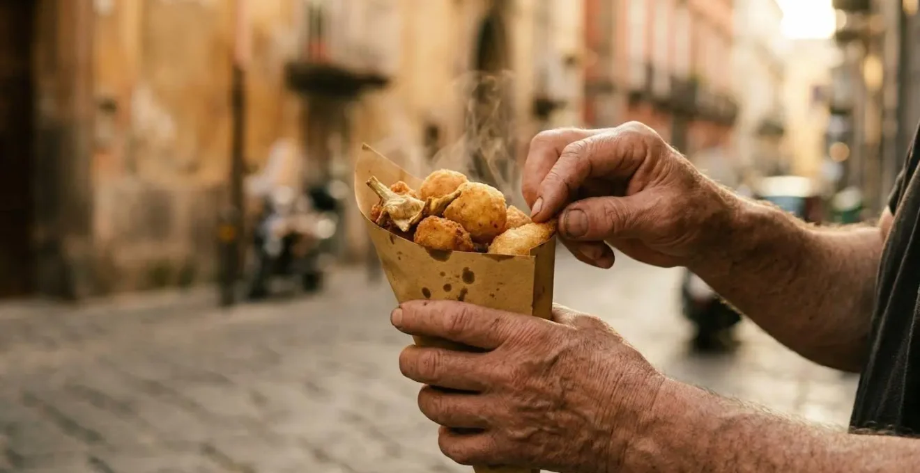 Mani che tengono un cuoppo di carta con fritti fumanti in una strada napoletana